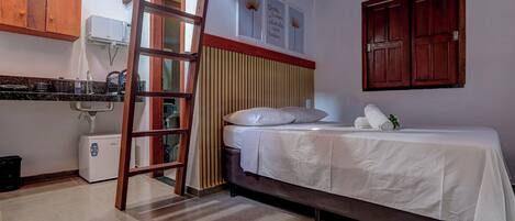A compact room with a bed, a small kitchenette, and a ladder leading to a lofted area.