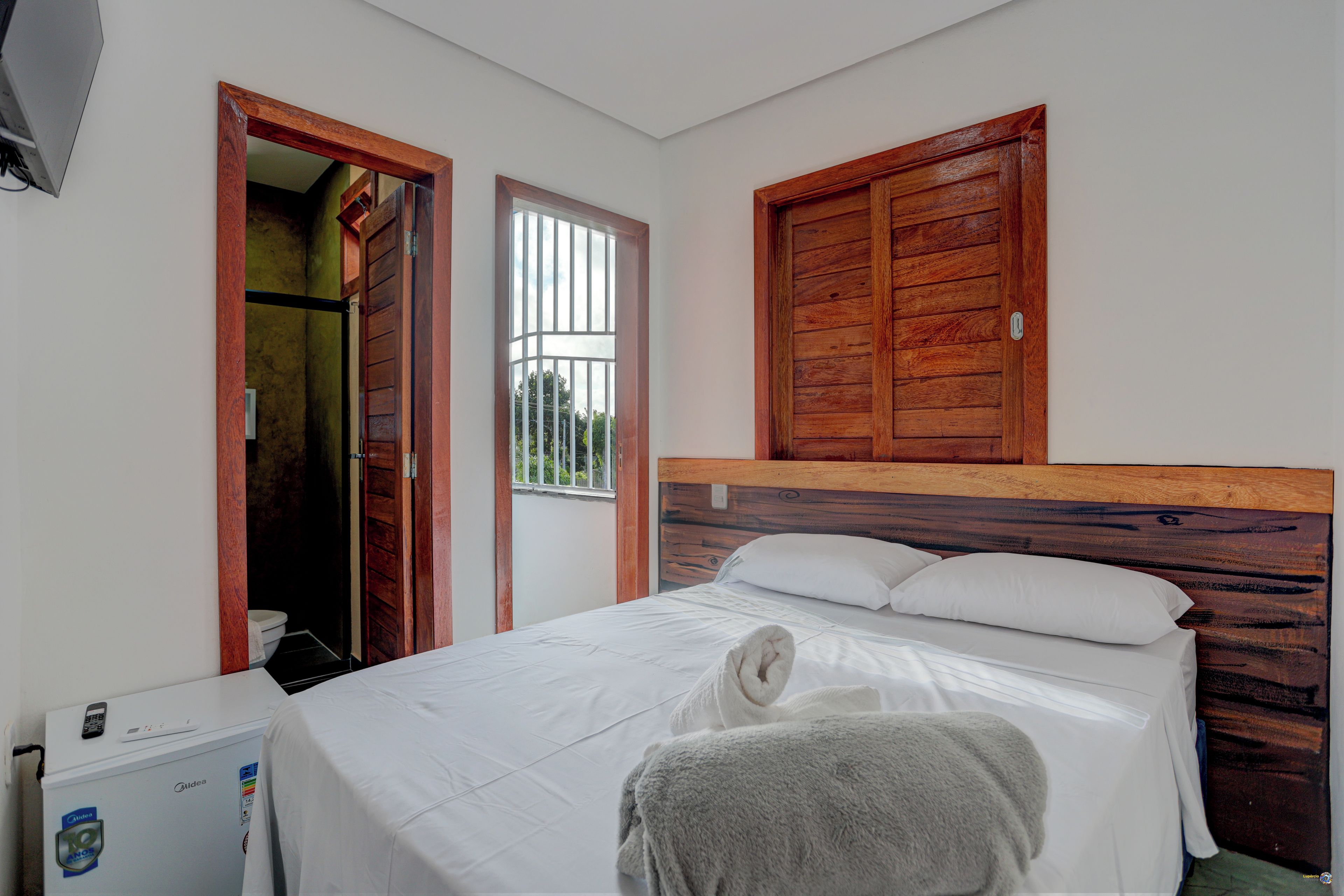 A bedroom with a bed, a wooden headboard, a window, and a door leading to a bathroom.