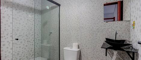 A bathroom with a glass shower enclosure, a toilet, a sink with a black basin, and a mirror above the sink.