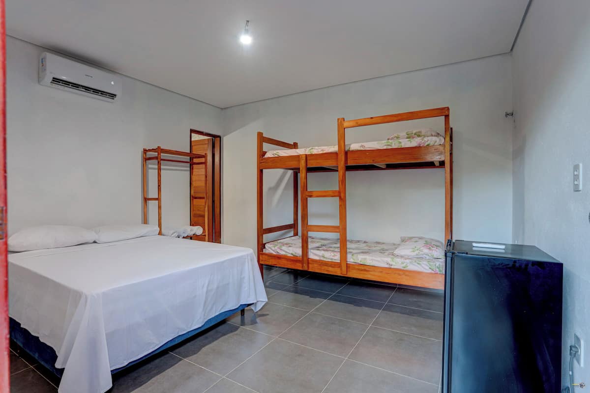 A room with a single bed, a bunk bed, a small table, and a refrigerator.