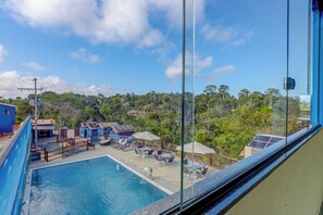 A swimming pool with lounge chairs and umbrellas, surrounded by buildings and trees. - Recanto Fiel (Itacaré)