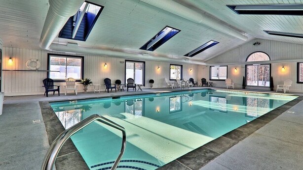 A large indoor swimming pool with multiple skylights, surrounded by lounge chairs and a poolside area. - 3BR/2BA, Ski in/out from A/B lift, pool & hot tub (Ludlow)
