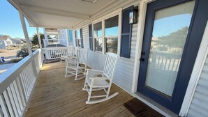 Une véranda couverte avec des fauteuils à bascule blancs et une porte bleue.