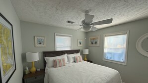 Une chambre à coucher avec un lit, des tables de chevet, un ventilateur de plafond et des tableaux encadrés accrochés aux murs.