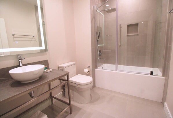 A modern bathroom with a large mirror, a white sink, a toilet, and a glass-enclosed shower area.