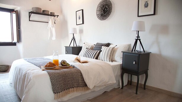 Un dormitorio ordenado con cama, mesitas de noche, lámpara y estante junto a la cama.