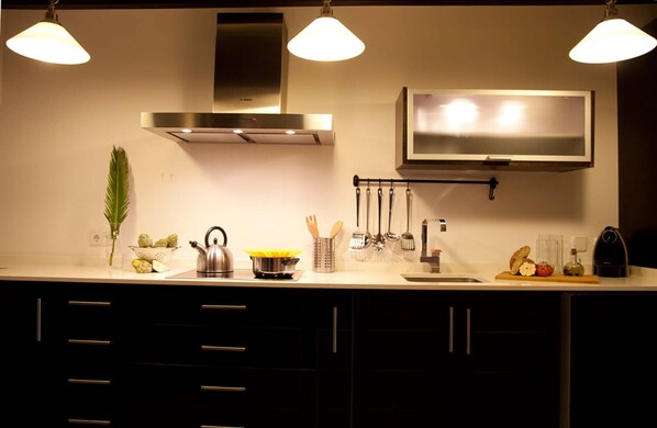 A modern kitchen with a stainless steel range hood, a microwave, and a sink. There are cabinets with black handles and a countertop with various kitchen items.