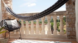 Un balcón con una hamaca, una silla con cojín estampado y vistas a viñedos.