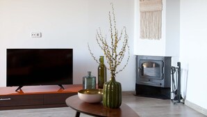 Una sala de estar moderna con un televisor de pantalla plana, una mesa de centro de madera con adornos, una chimenea y un adorno de macramé en la pared.