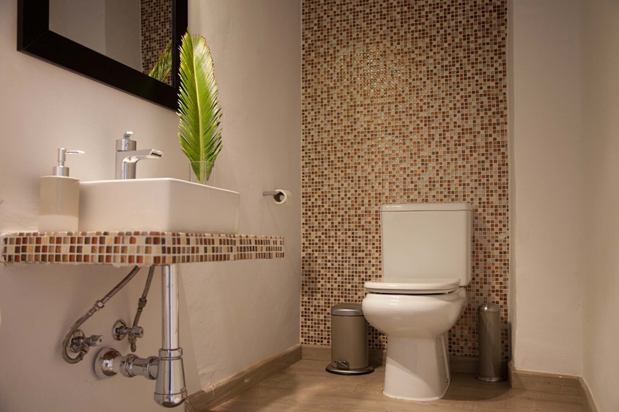 A bathroom with a white sink, a mirror, a toilet, and a trash can.