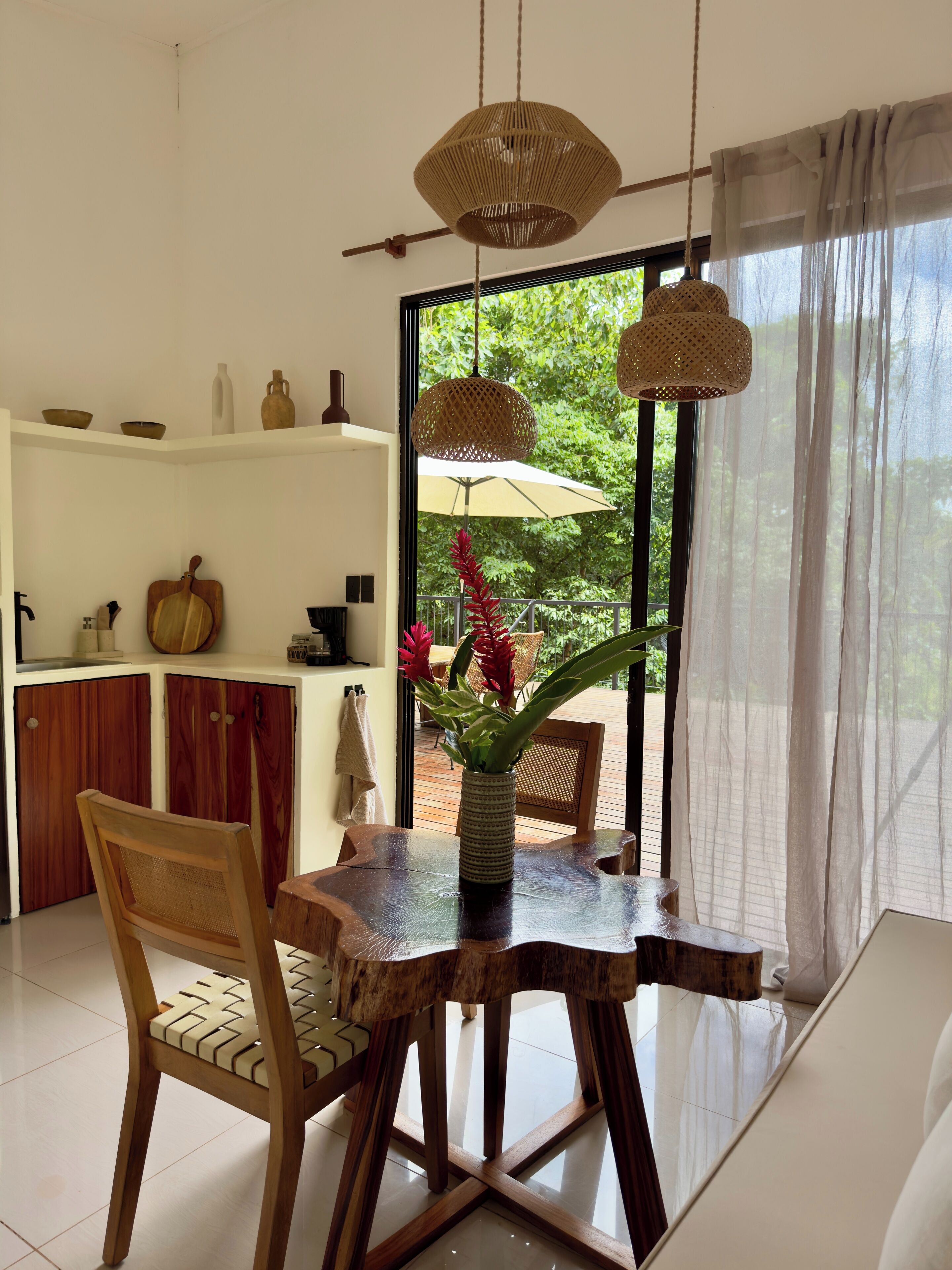 A dining area with a wooden table and chairs, a vase with flowers, and hanging woven light fixtures.