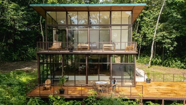 Une maison moderne en verre, dotée d’une terrasse en bois et d’un espace salon extérieur.
