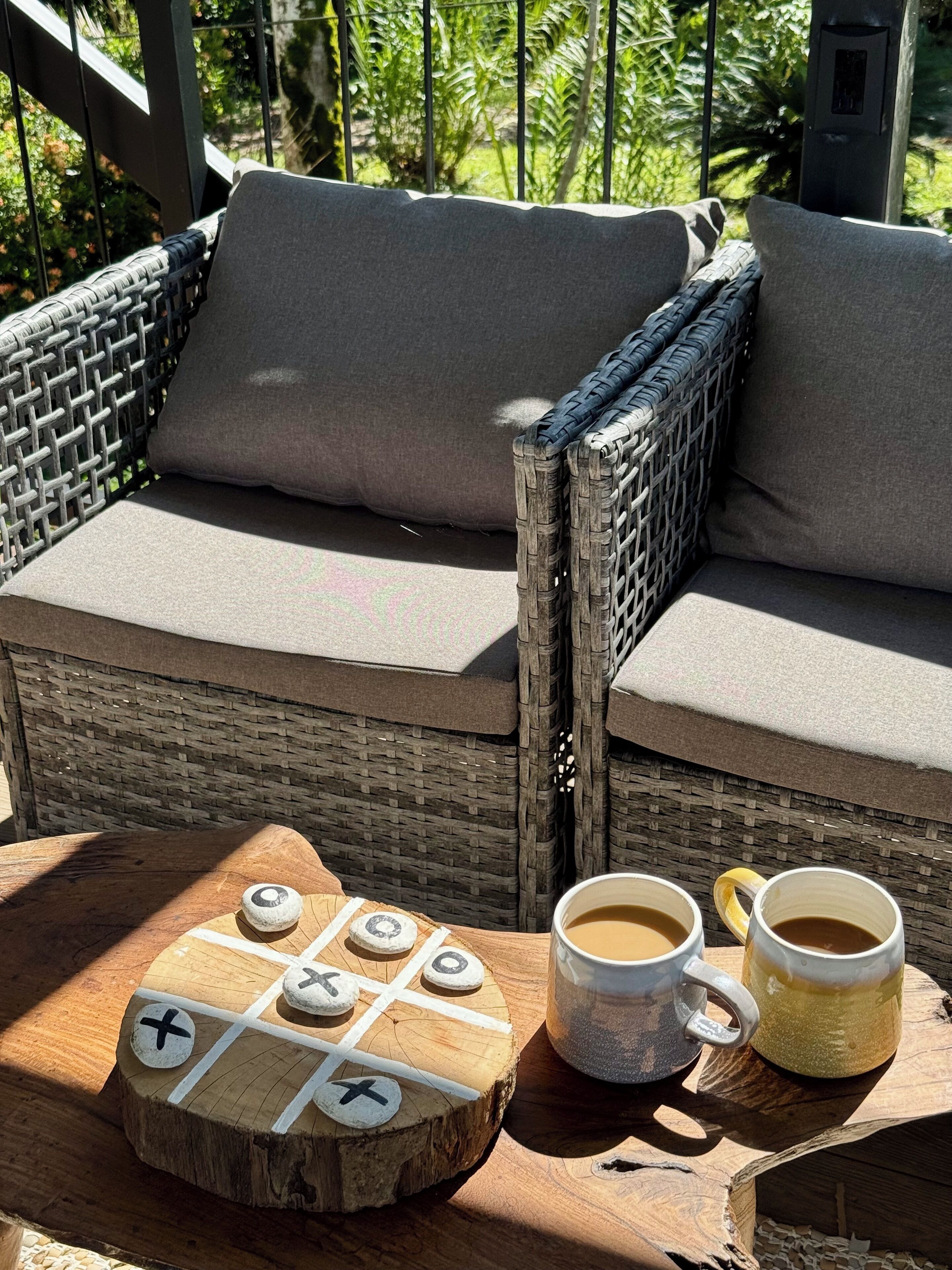 A wicker sofa with cushions, a wooden board game, and two mugs of coffee on a wooden table.
