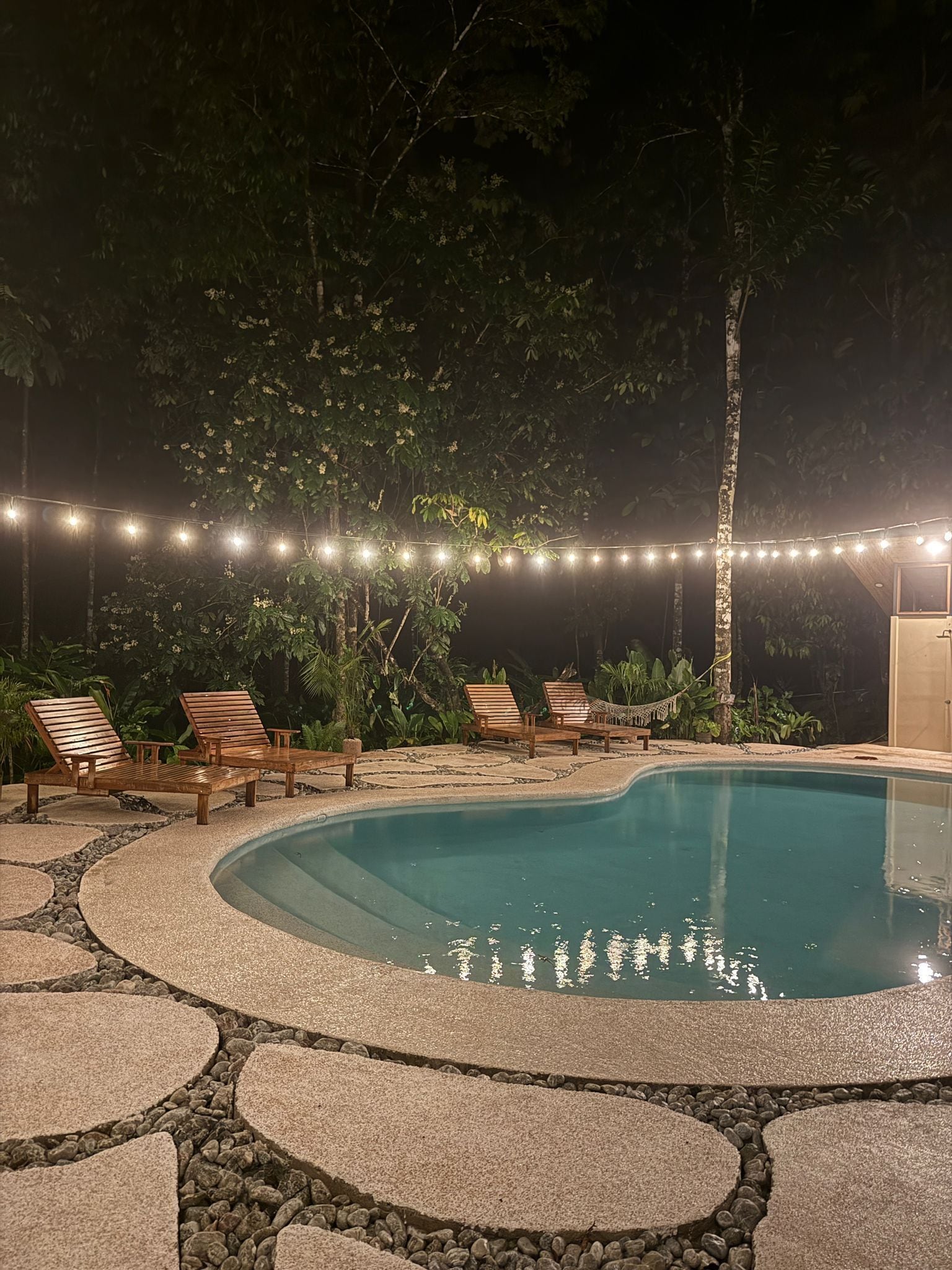 Un espace piscine agrémenté de chaises longues en bois et de guirlandes lumineuses.