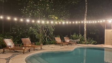 Un espace piscine agrémenté de chaises longues en bois et de guirlandes lumineuses.