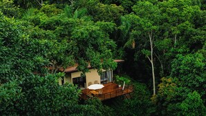 Un chalet isolé, entouré d’une forêt dense, doté d’une terrasse en bois et d’un petit porche.