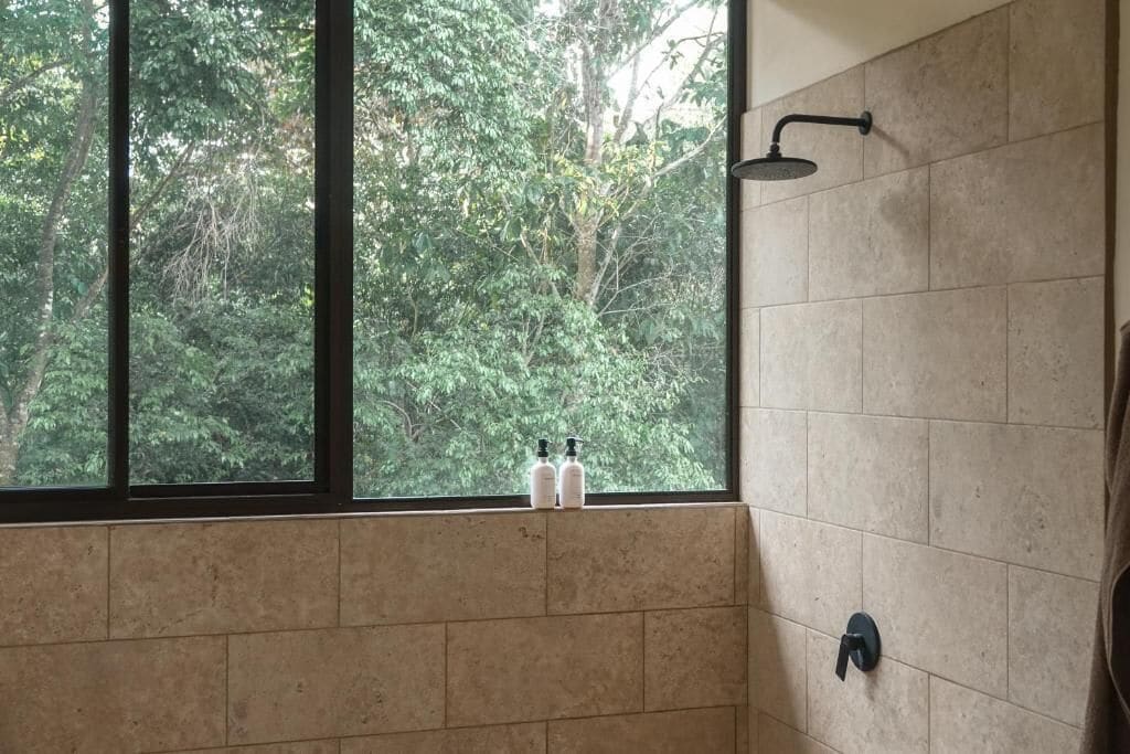 Un baño con ventana, ducha y dos botellas en el alféizar.