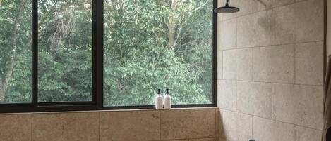 Un baño con ventana, ducha y dos botellas en el alféizar.