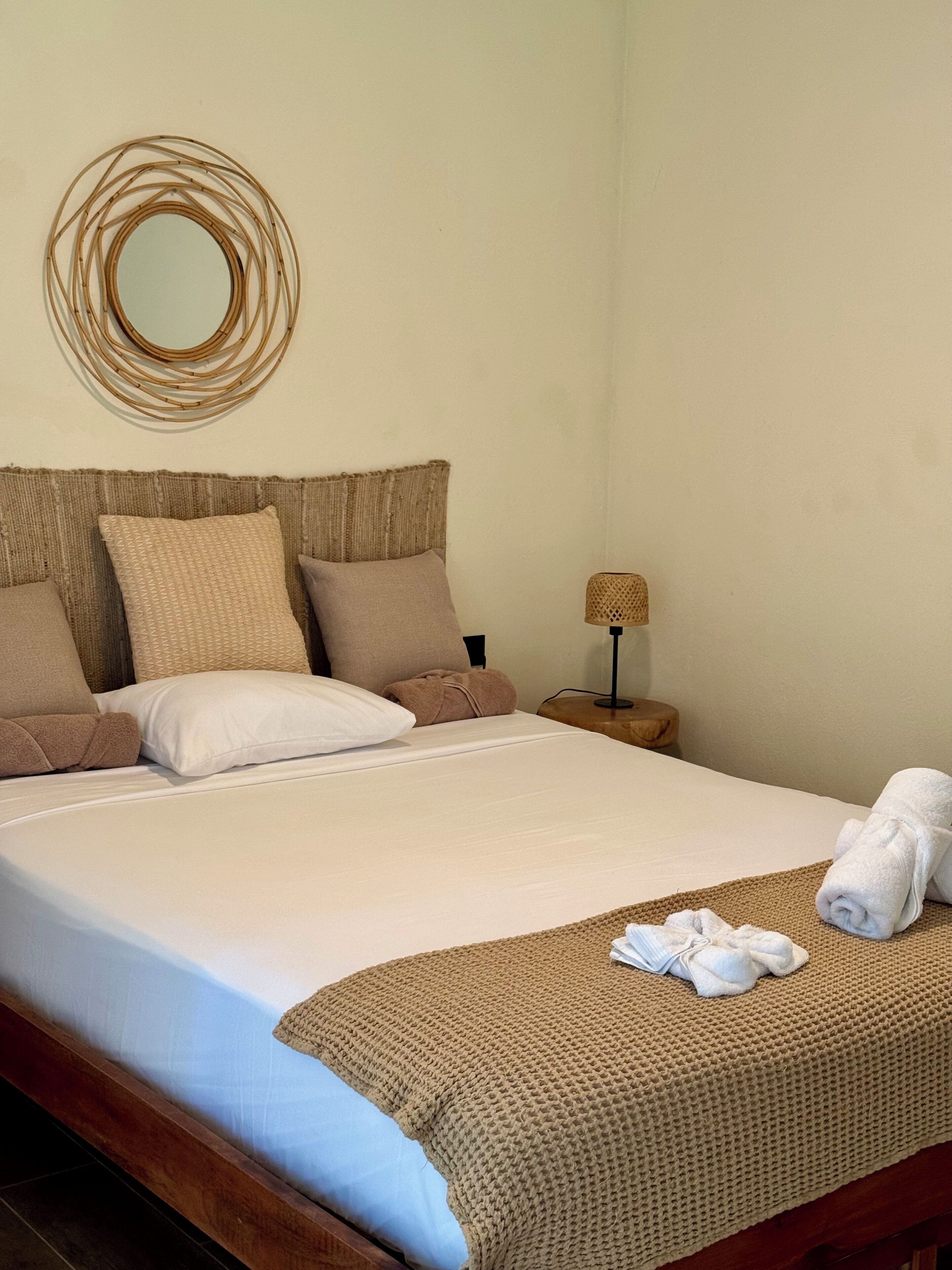 Uma cama bem arrumada com um cobertor branco e castanho, um xale de tricô marrom e uma toalha dobrada ao lado.