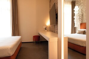 Una camera d'albergo con un letto, uno sgabello rosso, un comodino bianco, uno specchio e una parete in mattoni.