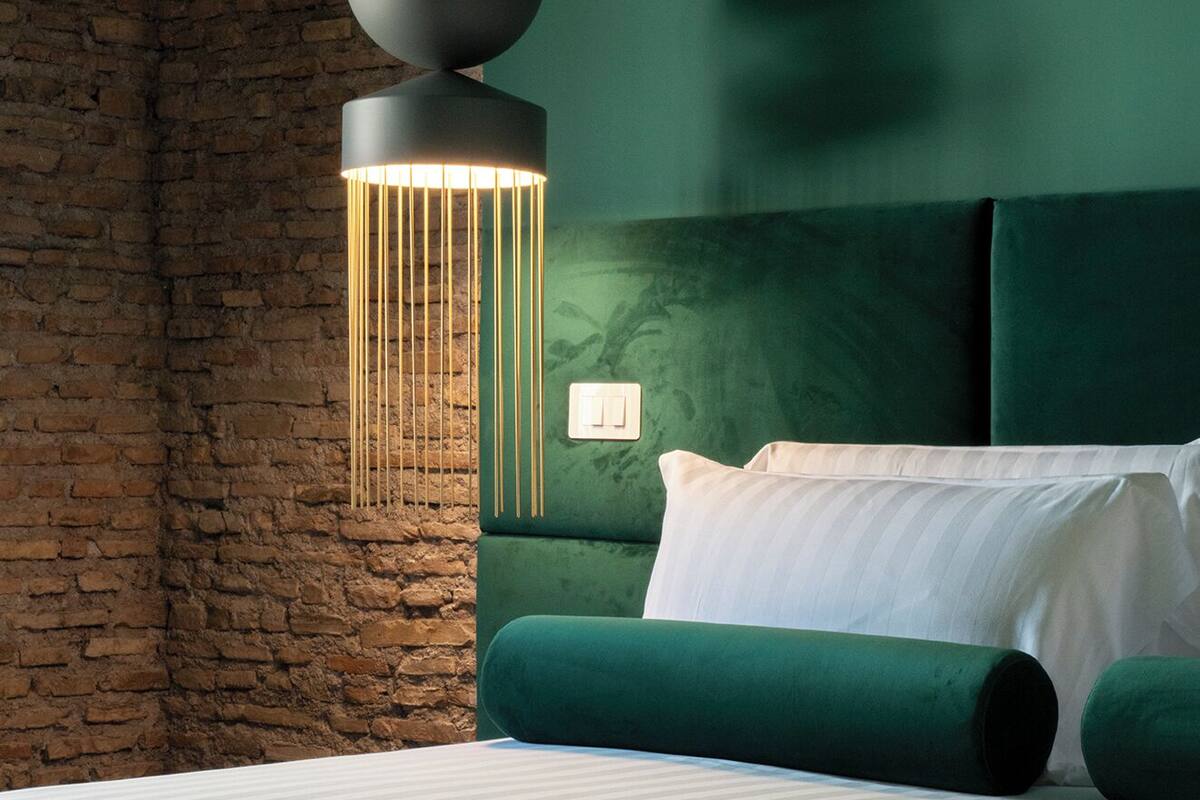 Ein modernes Schlafzimmer mit Backsteinwand, grünem gepolsterten Kopfteil, einem Bett mit weißer Bettwäsche und einer einzigartigen Pendelleuchte.