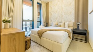 A bedroom with a large bed, a nightstand, a wooden dresser, and a view of the outside balcony. - Charming 1BR in Dania 3 IMPZ by Deluxe Holiday Homes (Dubai)
