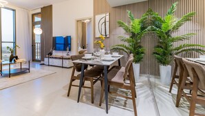 A modern dining area with a table set for four, surrounded by chairs. There is a large potted plant to the right, and a television mounted on the wall. - Charming 1BR in Dania 3 IMPZ by Deluxe Holiday Homes (Dubai)