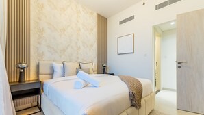 A modern bedroom with a large bed, bedside lamps, a wooden door, and a framed picture on the wall. - Charming 1BR in Dania 3 IMPZ by Deluxe Holiday Homes (Dubai)