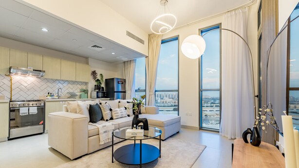 A modern living room with a sofa, coffee table, and a view of the city through large windows. - Charming 1BR in Dania 3 IMPZ by Deluxe Holiday Homes (Dubai)