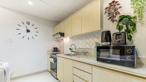 A modern kitchen with a wall clock, a microwave, a toaster, and a sink. - Charming 1BR in Dania 3 IMPZ by Deluxe Holiday Homes (Dubai)