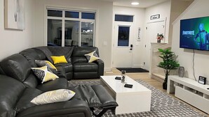 A modern living room with a sectional sofa, a white coffee table, and a flat-screen TV displaying Fortnite. - Stylish New Home, Near Shops, WiFi, 2V Garage, Smart TV, Private Yard, Near ✈️. (Edmonton)