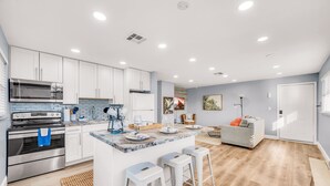 Une cuisine moderne avec des meubles blancs, un grand îlot central doté de tabourets, des appareils électroménagers en acier inoxydable et un plancher en bois.