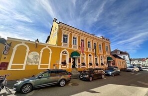 A yellow building with a green entrance, parked cars, and a clear sky.