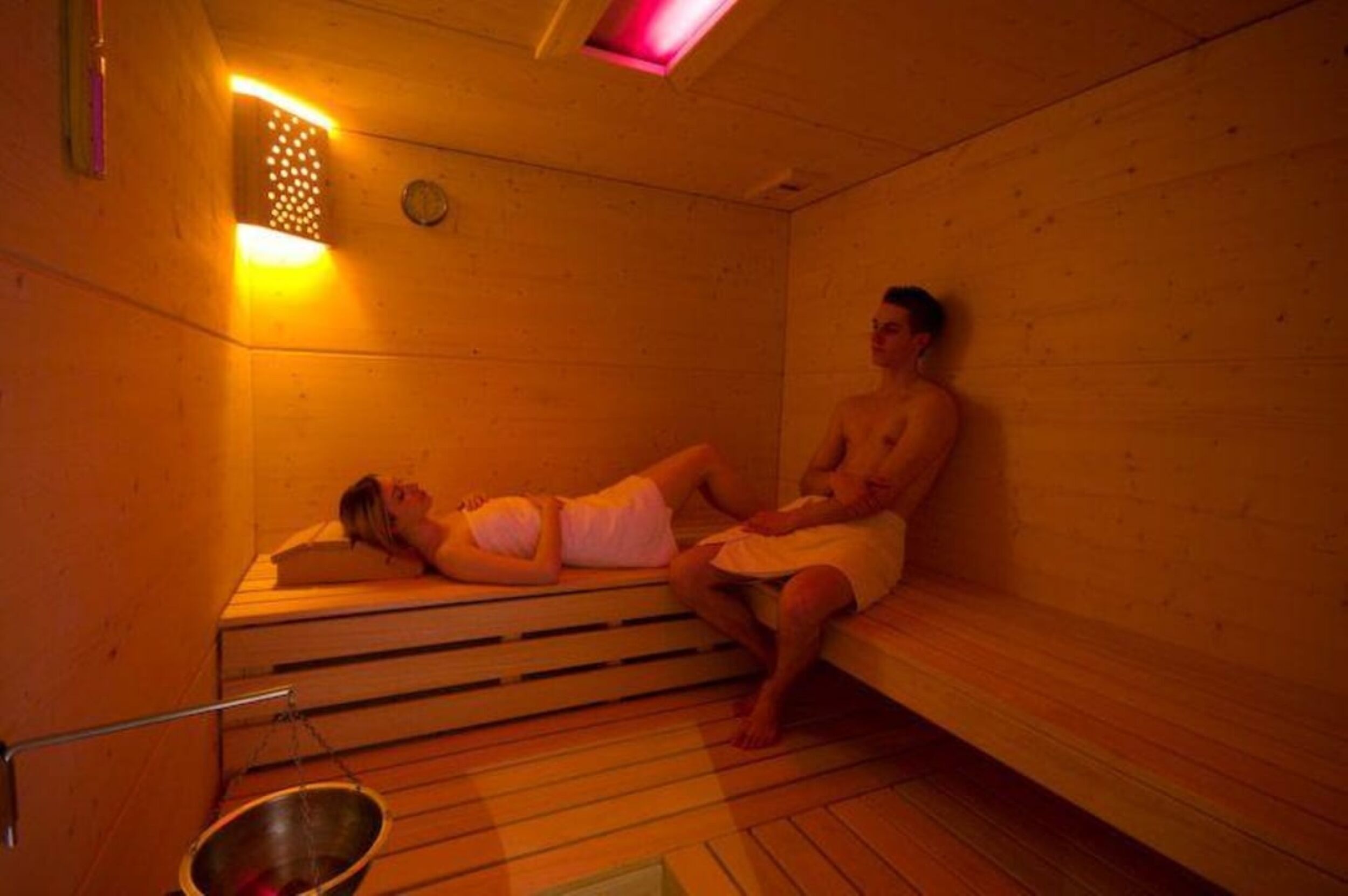 A sauna room with wooden benches and a metal basin.