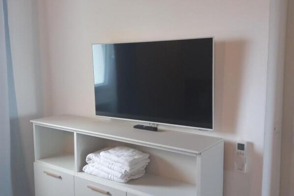 A white TV stand with a flat-screen TV mounted above it. Below the TV, there is a shelf with folded white towels. - GREEN SEA RELAX - in the hills surrounding the city and near the Cinque Terre (La Spezia)