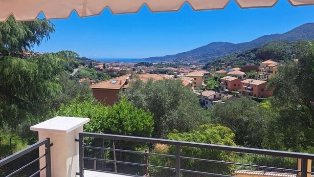 Un balcón con vistas a un pueblo costero, rodeado de vegetación y montañas.