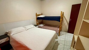 Une chambre avec un lit superposé, une tête de lit en bois, un lit simple avec un matelas blanc et une porte sur le côté droit.
