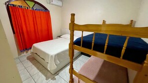 A small, simple room with a wooden bunk bed, a single bed with a white mattress, a red curtain, and a white wall with a small air conditioning unit.
