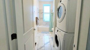 A laundry room with stacked washers and dryers, a window with a view, and a tiled floor.