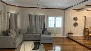 A spacious living room with a large gray sectional sofa, a wooden floor, and a ceiling fan.