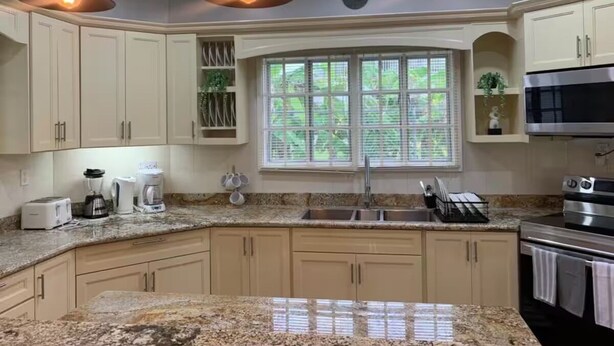 A kitchen with light-colored cabinets, a granite countertop, a built-in oven, a microwave, and pendant lighting.