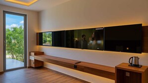 Ein modernes Zimmer mit einem großen Fenster, einem integrierten Fernseher, einer hölzernen Sitzbank und einem Wasserkocher auf einem kleinen Tisch.