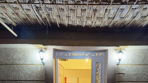 A hotel entrance with a checkered floor, a thatched ceiling, and two potted plants.