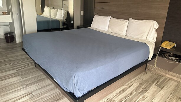 A modern hotel room with a large bed, wooden flooring, a bedside telephone, and a mirror. - Blue Diamond Inn (Houston)