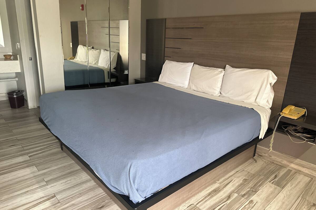 A modern hotel room with a large bed, wooden flooring, a bedside telephone, and a mirror.