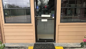 A building entrance with a yellow tactile paving mat, a black door with a glass panel, and two black wall-mounted lights. - Blue Diamond Inn (Houston)