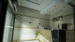 Un área de recepción con mostrador de mármol, una planta en maceta y cuadros en la pared.