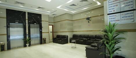 A spacious lobby with a marble floor, a reception desk, two elevators, and a seating area with sofas.