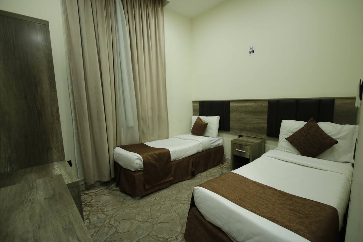 Hotellihuone, jossa on kaksi sänkyä, yöpöytä, puinen pääty ja verho.