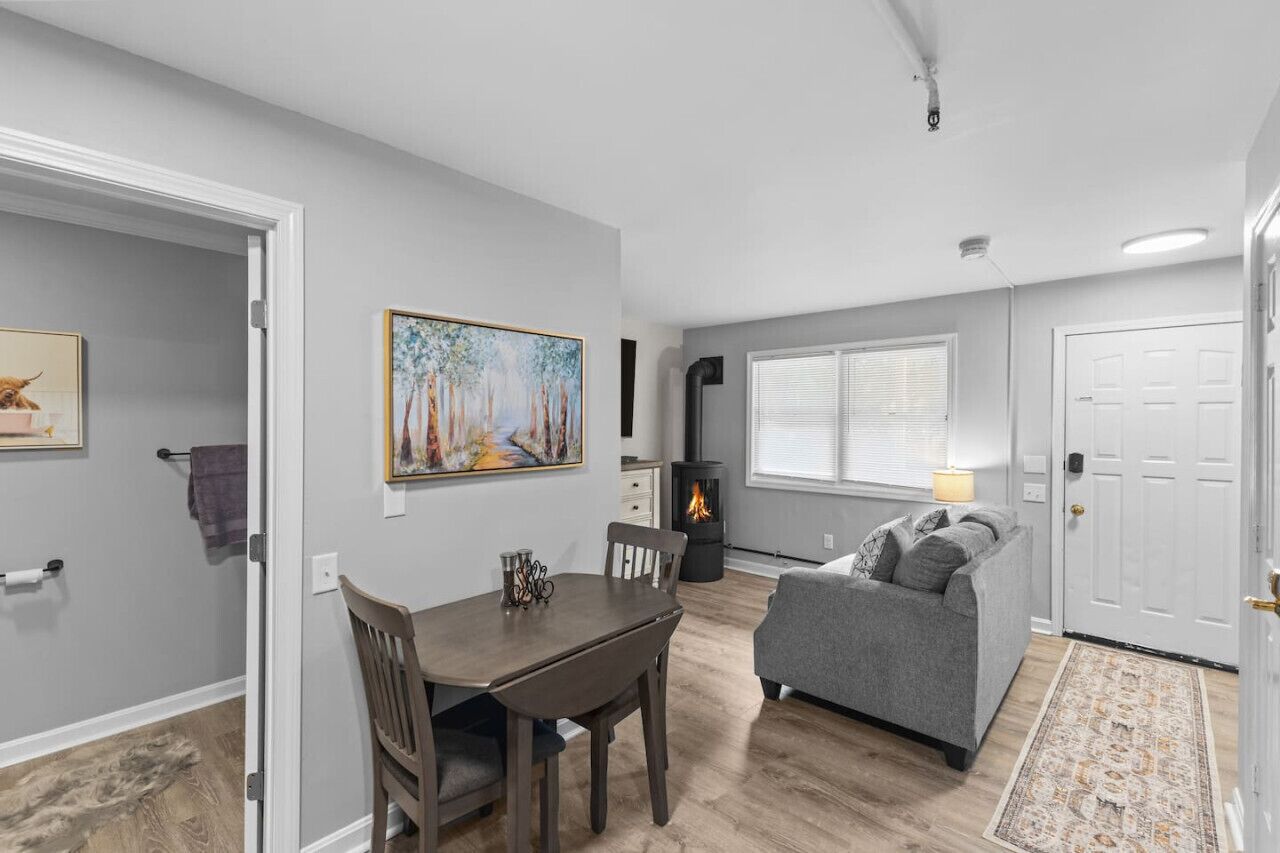 A living room with a fireplace, a dining area with a table and chairs, and a gray sofa.